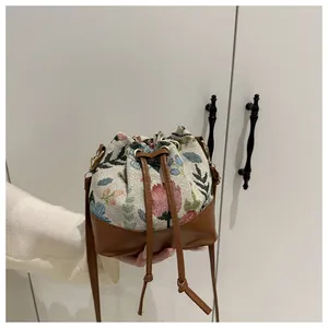 Detailed close-up of floral embroidery fabric and brown leather on drawstring bucket bag
