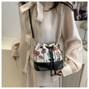 Close-up of floral jacquard and black leather bucket bag with drawstring and tassels