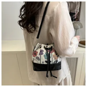Detail view of floral print canvas drawstring bucket bag with black leather shoulder strap