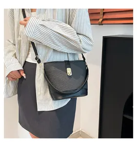 Close-up of a black textured bucket bag with a golden metal twist-lock on a striped shirt