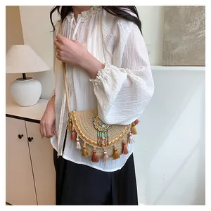 Dettaglio della borsa a tracolla in paglia boho con nappe colorate e conchiglie su modella