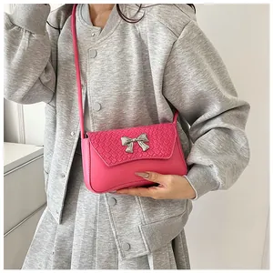 Close-up of pink crossbody bag with woven texture flap and silver metal bow detail