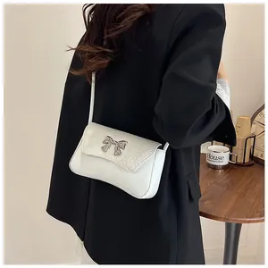 Detail of white crocodile-embossed shoulder bag with a silver bow buckle on a model