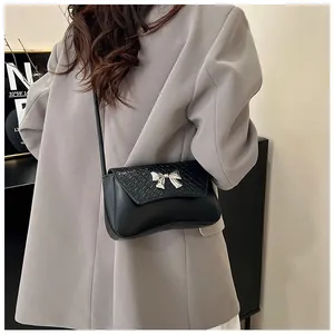 Detail of black faux leather shoulder bag featuring a silver metal bow buckle