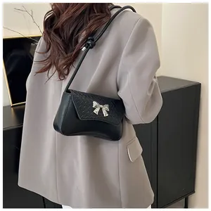 Detail of black matte leather shoulder bag with woven texture and silver bow buckle