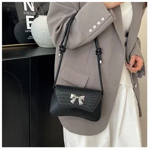 Detail of black woven texture shoulder bag with silver bow buckle worn by a model