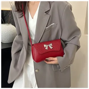 Close-up of a stylish red leather crossbody bag featuring a silver bow buckle and textures
