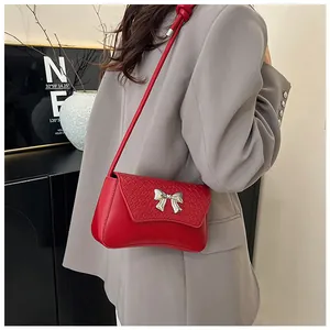 Red crocodile embossed shoulder bag with silver bow buckle worn by a model in casual style