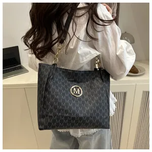 Détail du sac cabas noir avec motif M et bandoulière chaîne dorée porté par un mannequin