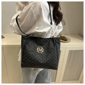 Détail du sac cabas noir à motif M et logo doré porté à l'épaule par le modèle