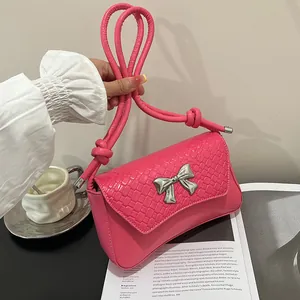 Pink shoulder bag with woven flap, silver bow, and knotted strap held by model