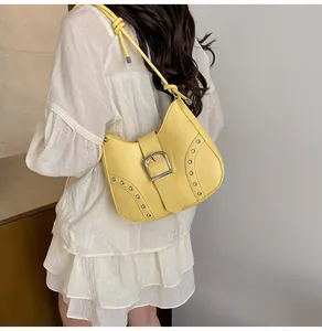 Detail of yellow shoulder bag featuring silver grommets and buckle closure on model