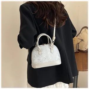 Detail of shell-shaped crossbody bag with floral embossed texture and golden hardware