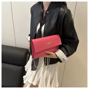 Detail of rose red PU leather crossbody bag with golden bow and elegant chain strap