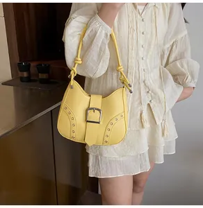 Close-up of bright yellow shoulder bag with silver eyelets and buckle on white dress