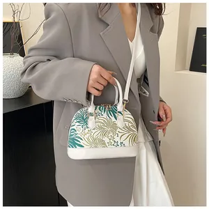 Detail of shell-shaped white handbag featuring tropical palm embroidery and zipper closure