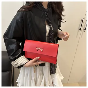 Detail of red envelope crossbody bag with gold bow clasp and metallic chain strap