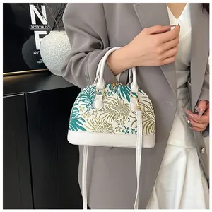 Detailed embroidery of green and gold floral patterns on ivory shell-shaped handbag