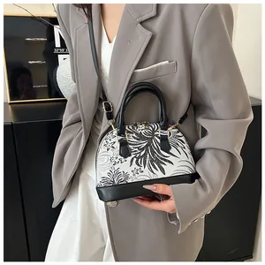 Detail of shell-shaped handbag featuring black and white botanical prints and gold hardware