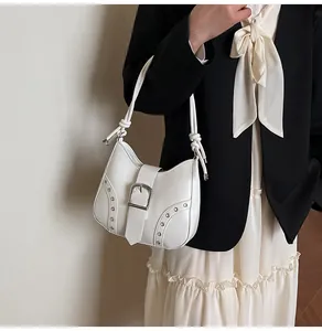 Detailed shot of white leather crescent shoulder bag with silver buckle and metal studs