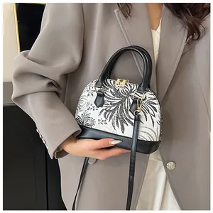 Detail of white shell-shaped handbag with black floral print and gold hardware