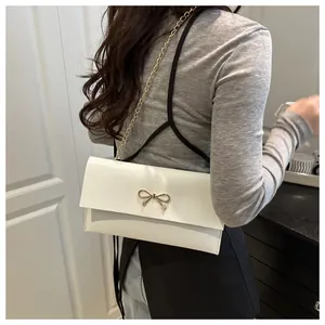 Detailed shot of white envelope crossbody bag with gold bow clasp and chain strap