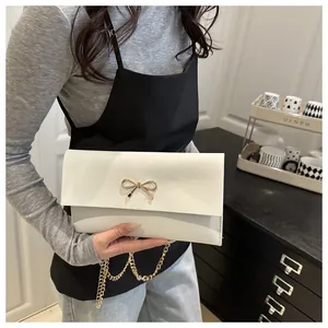 Detail of white leather envelope bag featuring a gold metal bow clasp and chain strap