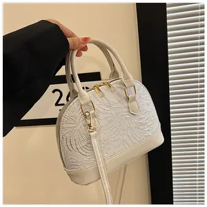 Detail of white shell-shaped handbag showing silver floral embroidery and golden zippers