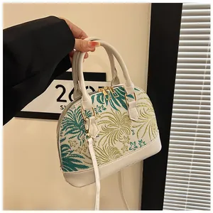 Detail of white shell handbag featuring tropical floral embroidery and golden metal hardware