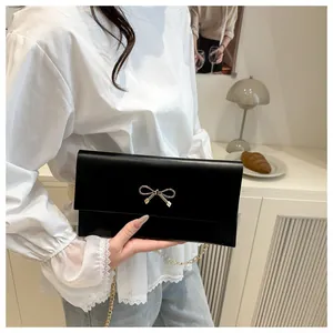 Close-up of black envelope bag featuring matte leather texture and gold bow clasp