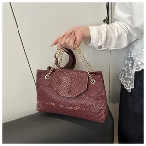 Detail of burgundy snakeskin embossed tote with gold chain strap held by a model