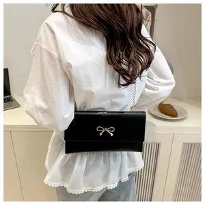 Close-up of black crossbody bag with gold bow clasp worn by model in a cozy indoor setting