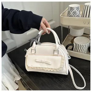 Detail of white faux leather crossbody bag with lace trim and checkered bow charm