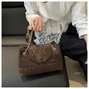 Brown snakeskin pattern tote bag with gold chain strap shown on person in white shirt