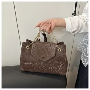 Detail of snake skin pattern tote bag with gold chain strap in hand carry scene