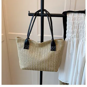Detail of herringbone weave texture and black shoulder strap on straw tote bag