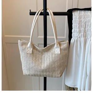 Detail of cross-stitched leather handles on a beige woven straw tote bucket bag