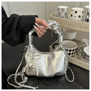 Close-up of silver crescent handbag with pleated handle and pearl bow detail
