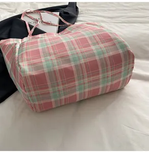 Detail of pink and green plaid nylon tote bag on white bedding with a black blazer