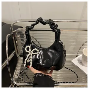 Macro detail of black leather bag with pearl bow pendant and metal chain strap