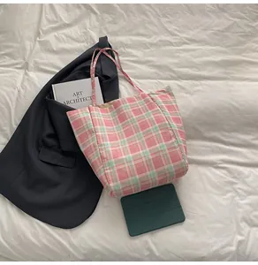 Vue à plat d'un cabas en nylon à carreaux rose et vert sur lin avec blazer et livre