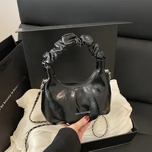 Fashionable black glossy crossbody bag with pleated handle and silver chain strap on a gift box