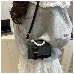 Detail of a black textured crossbody bag featuring a large pearl handle and leather strap