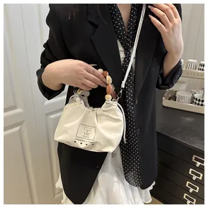 Detalle de bolso bandolera de lona con asa de cuentas y estampado de oso visto en modelo