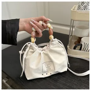 Detalle de bolso beige ajustable con asa de cuentas jaspeadas y gráfico de osito sutil
