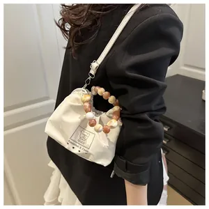 Detalle del bolso plisado crema con asa de cuentas y etiqueta decorativa de marca