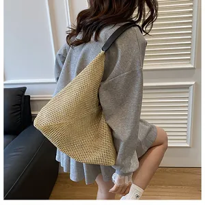 Close-up of woven straw shoulder bag with black leather straps on a model in casual wear