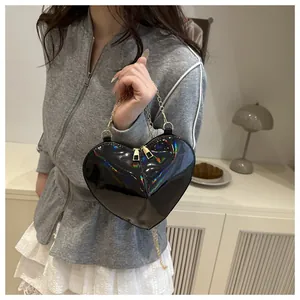 Detail of a black heart-shaped handbag with holographic finish and gold chain strap