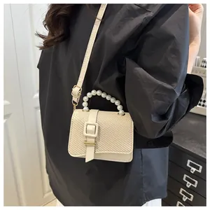 Detail of a creamy white mini square bag featuring woven texture and a pearl bead handle