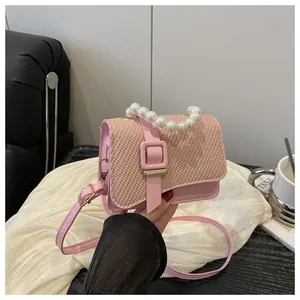 Detail of pink pearl handle on woven flap crossbody bag with golden chain and clasp